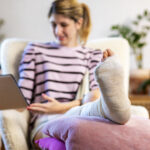 Young woman with leg in plaster using digital tablet