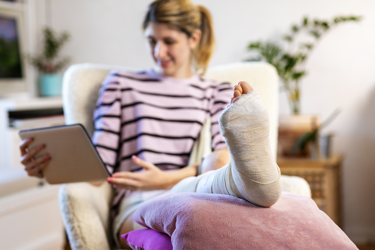 Young woman with leg in plaster using digital tablet