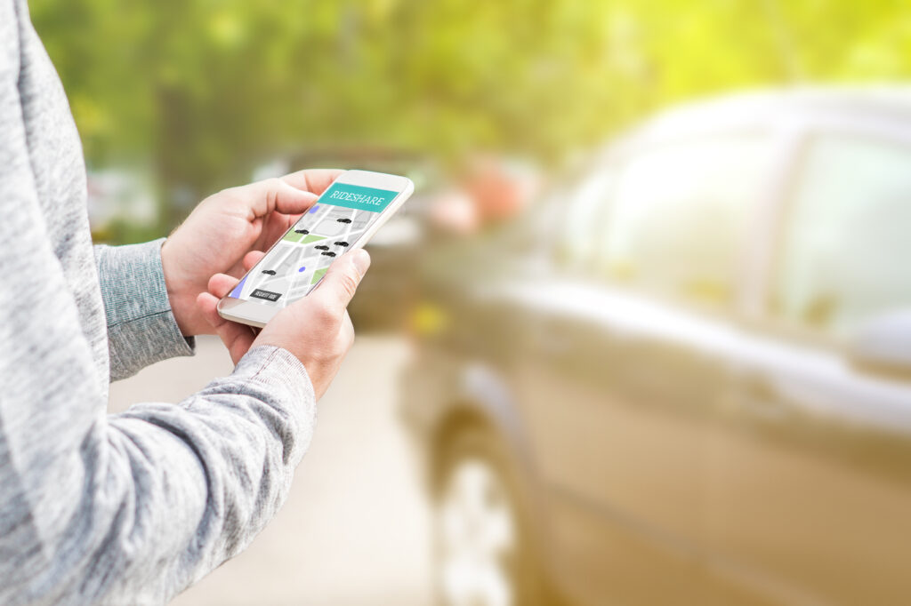 Man holding phone looking at rideshare app with a car in background